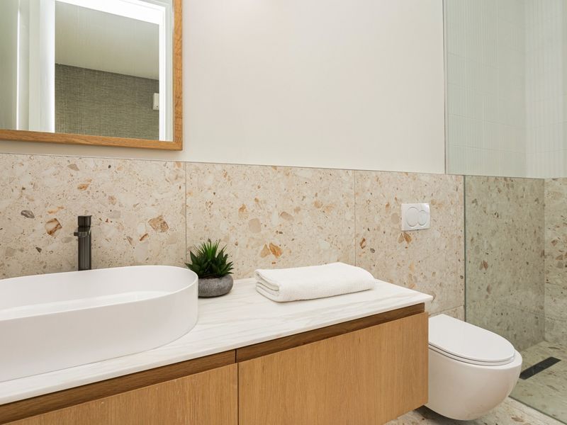 Modern bathroom featuring a floating vanity with vessel sink, terrazzo wall tiling, wall-hung toilet, and a glass-enclosed shower area.