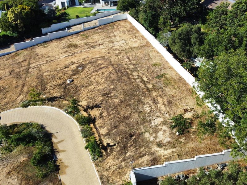 An aerial view of a vacant residential plot featuring a paved driveway, perimeter boundary walls, and established surrounding vegetation.