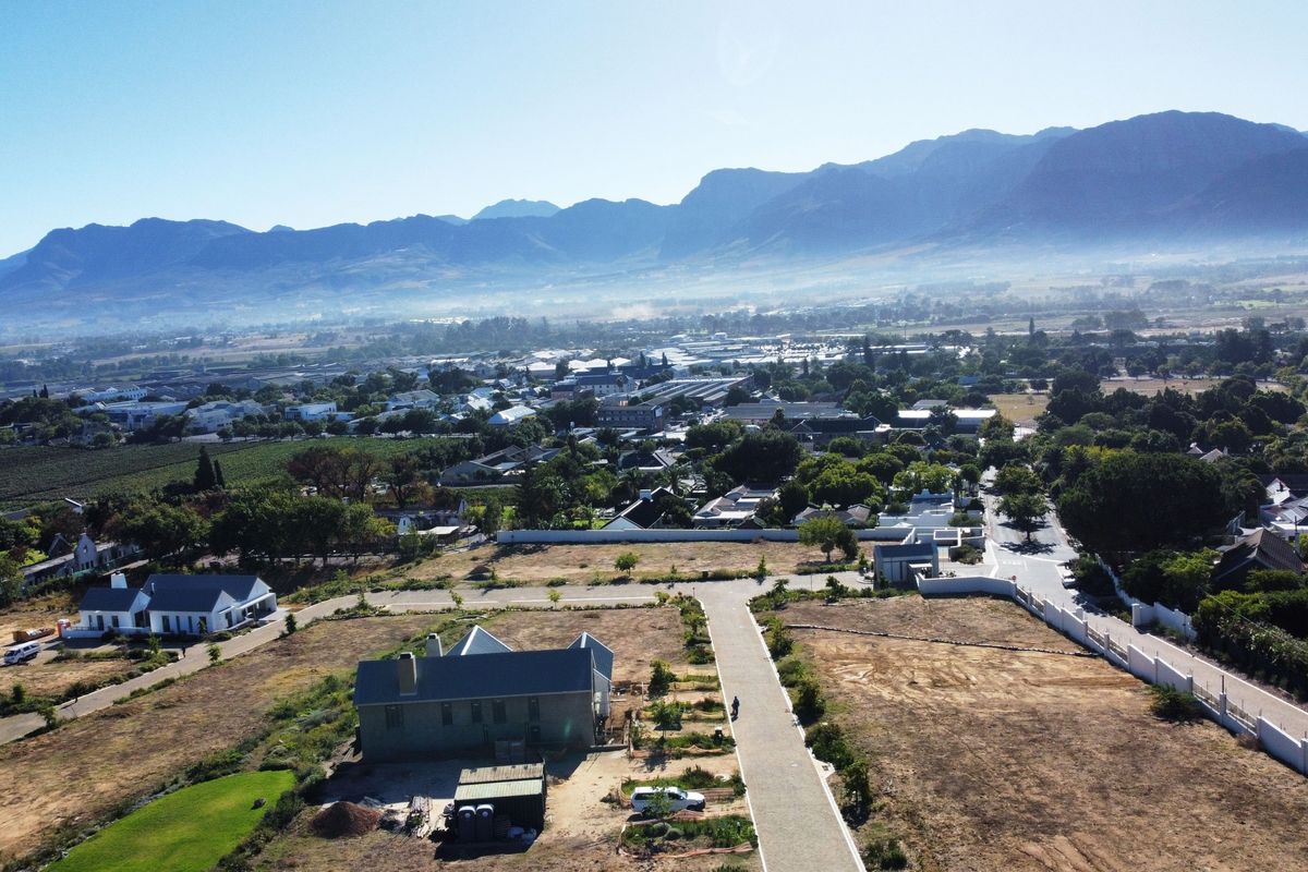 Aerial view of a residential development area featuring paved roads, boundary walls, and surrounding landscape with mountain views.