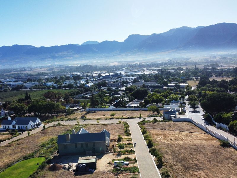 Aerial view of a residential development area featuring paved roads, boundary walls, and surrounding landscape with mountain views.