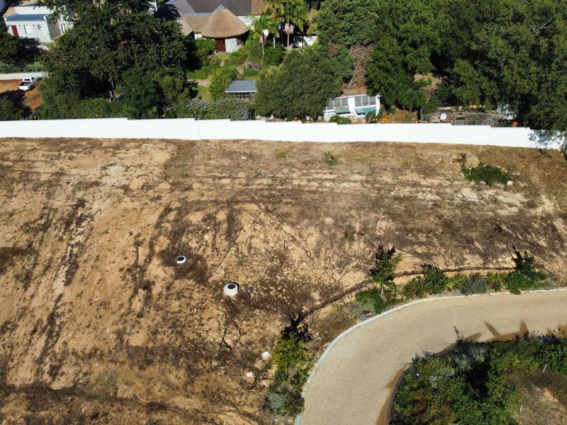 Aerial view of a vacant residential plot featuring a perimeter wall and paved driveway access.