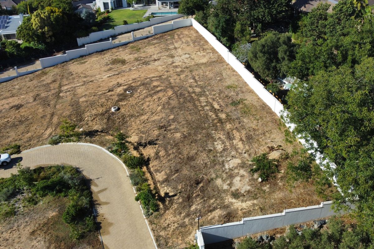 Aerial view of a vacant residential plot featuring a paved driveway, perimeter boundary walls, and established surrounding trees.