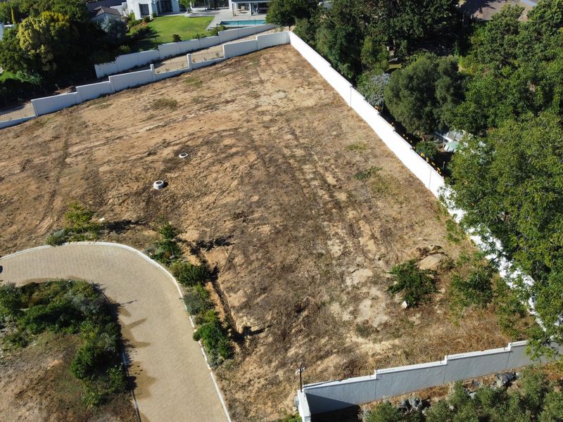 Aerial view of a vacant residential plot featuring a paved driveway, perimeter boundary walls, and established surrounding trees.