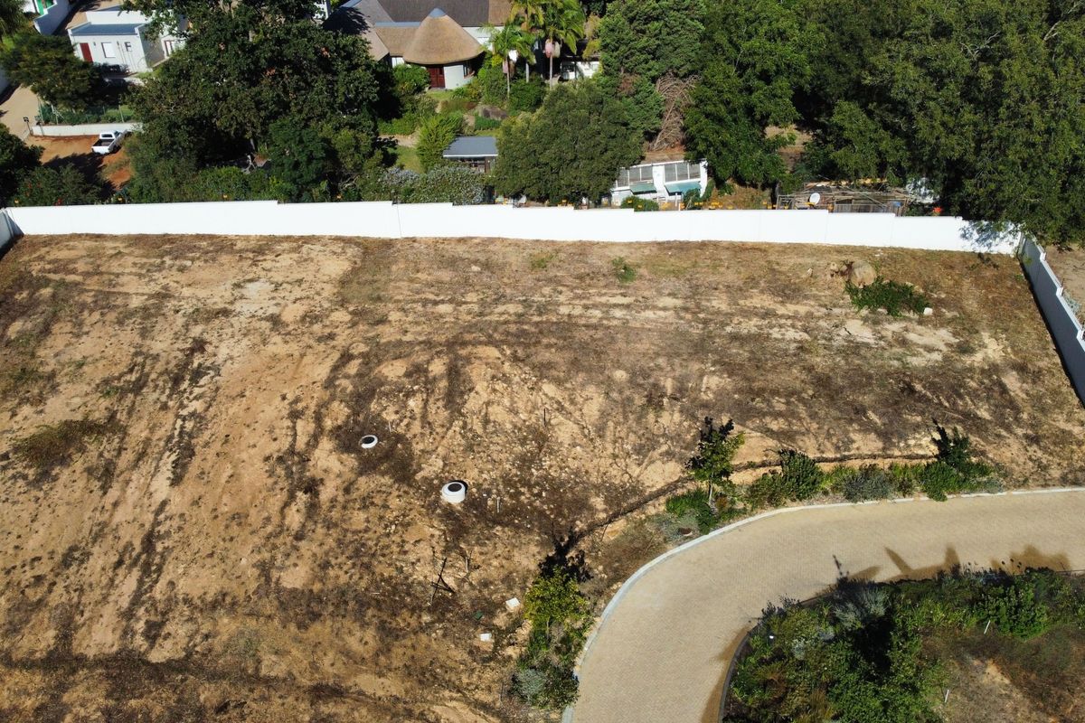 Aerial view of a vacant residential plot featuring a perimeter wall and paved driveway access.