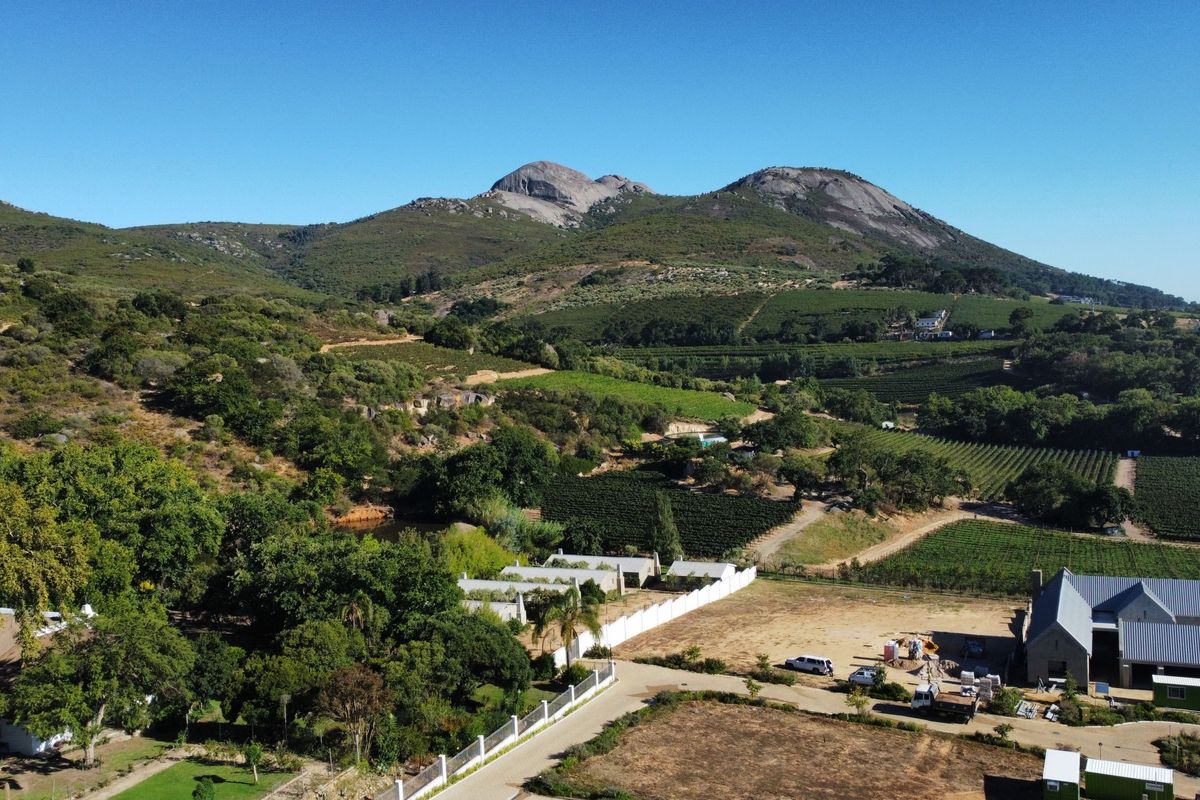 Aerial view of a residential property featuring expansive landscape, mountain backdrop, and existing building structures within a rural setting.