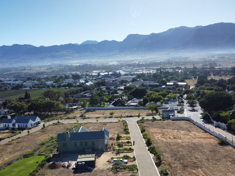 Aerial view of a residential development site featuring paved roads, boundary walls, and surrounding mountain landscape.
