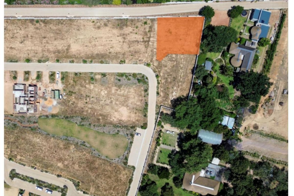 Aerial view of a vacant residential plot highlighted in orange, situated within a developed estate with established road access and surrounding greenery.