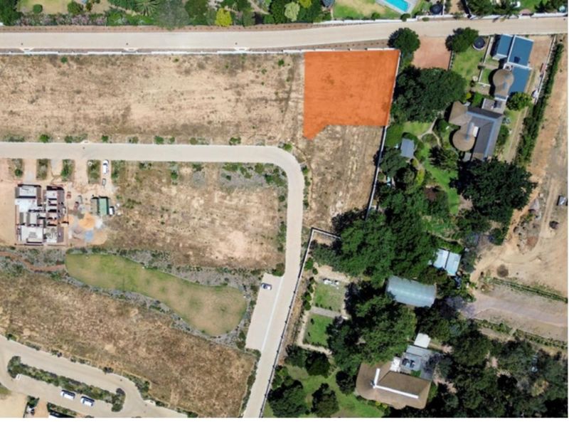 Aerial view of a vacant residential plot highlighted in orange, situated within a developed estate with established road access and surrounding greenery.