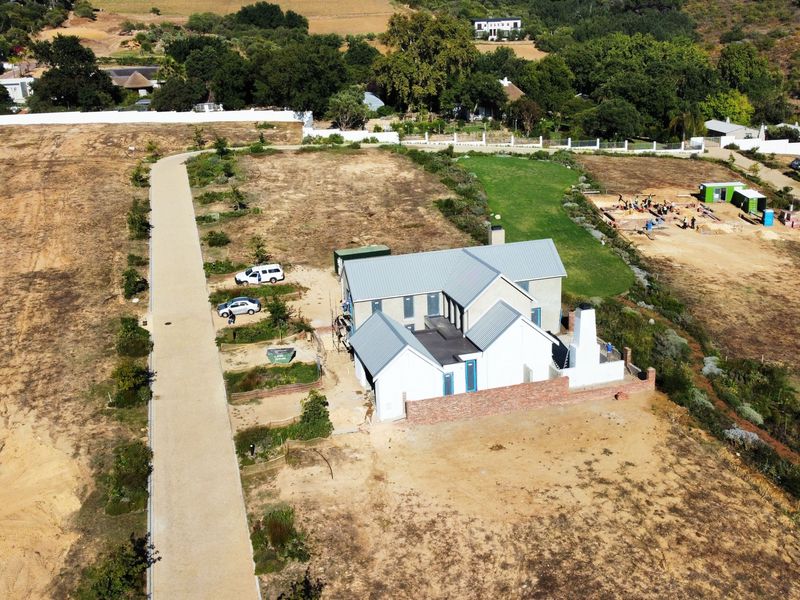 Aerial view of a residential property under construction, featuring a main dwelling with a metal roof, brick boundary wall, and surrounding vacant land.