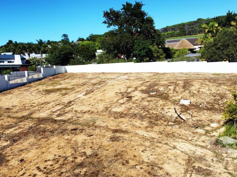 A vacant residential plot featuring a cleared surface, perimeter boundary walls, and established surrounding neighborhood vegetation.
