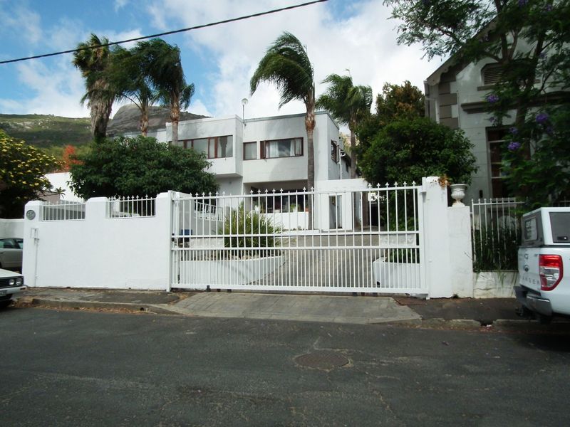 Front exterior view of a multi-level residence featuring a secure gated entrance, paved driveway, and established palm trees.