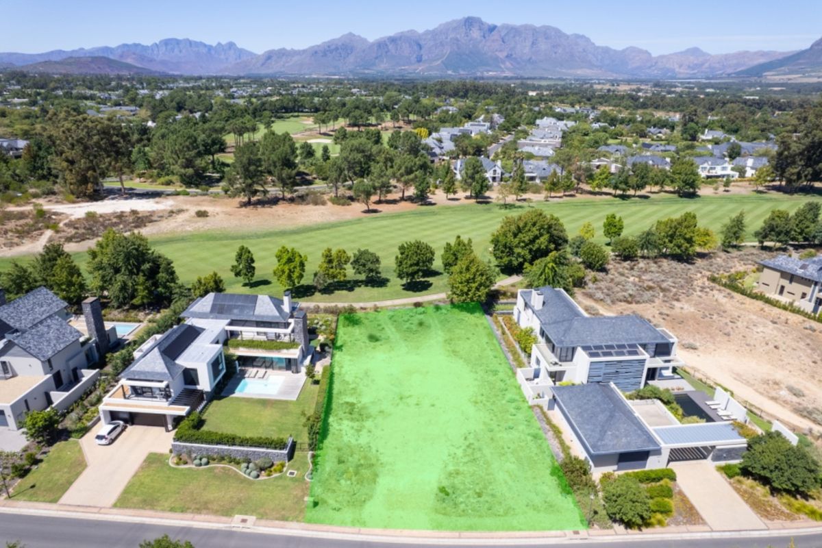 An aerial view of a vacant residential plot situated in a prime location, directly bordering a golf course with scenic mountain views.