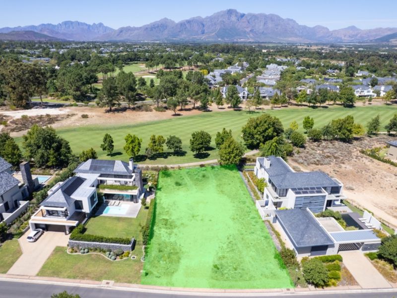 An aerial view of a vacant residential plot situated in a prime location, directly bordering a golf course with scenic mountain views.
