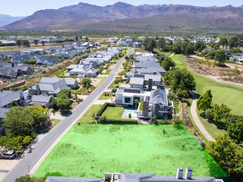 Aerial view of a vacant residential plot situated in a premium estate, adjacent to a golf course with scenic mountain views.