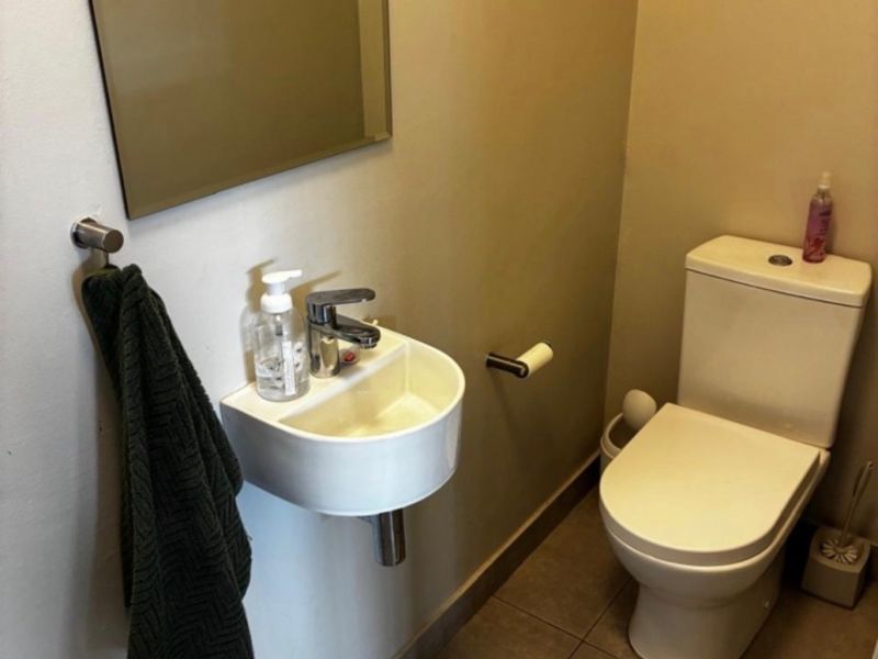A compact guest bathroom featuring a wall-mounted basin, a modern toilet, and neutral floor tiling.