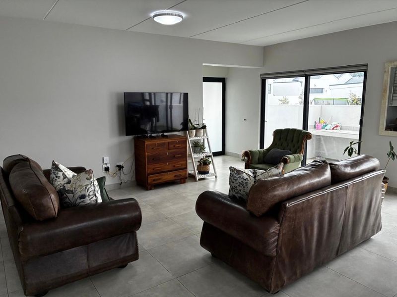 A spacious living room featuring neutral tiled flooring and large sliding glass doors that provide access to an outdoor patio area.