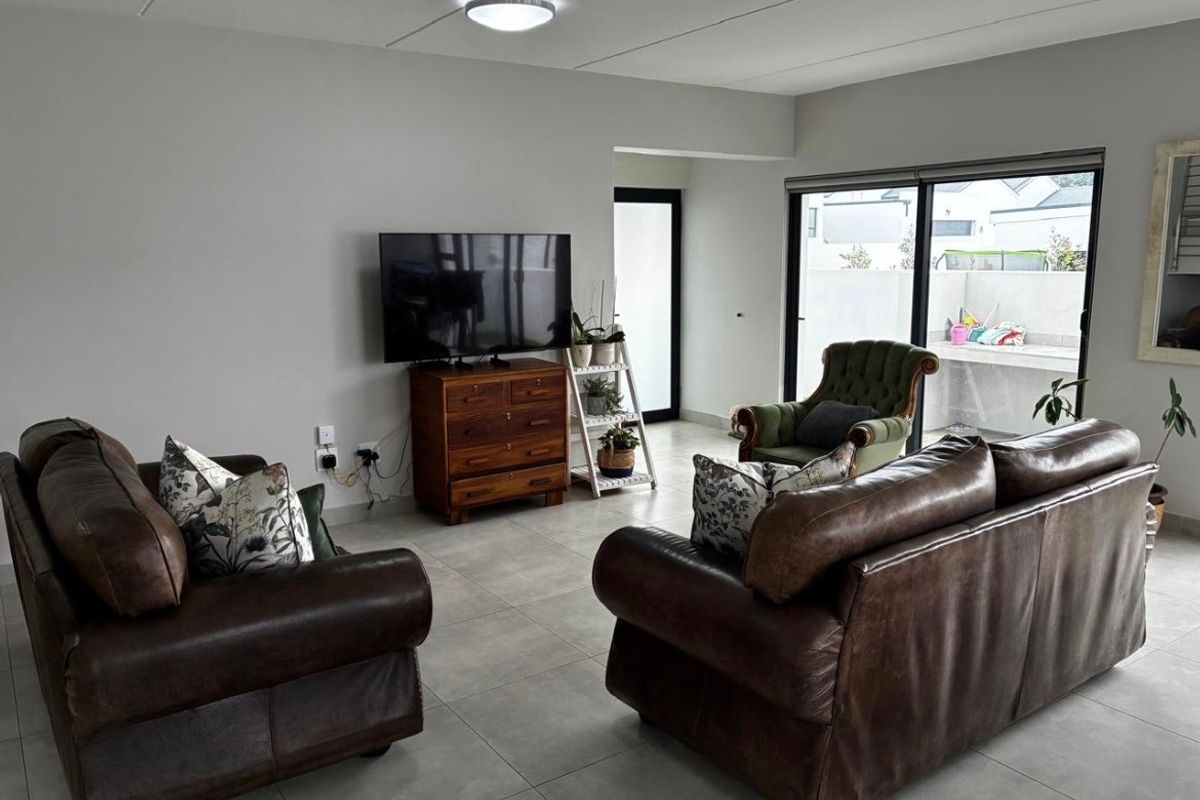 A spacious living room featuring neutral tiled flooring and large sliding glass doors that provide access to an outdoor patio area.