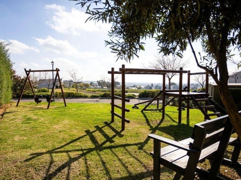 A well-maintained communal garden area featuring a lawn, mature hedging, and playground equipment with scenic views of the surrounding estate.