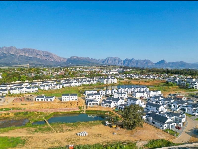 Aerial view of a residential townhouse estate featuring modern homes, landscaped ponds, and scenic mountain views in the background.