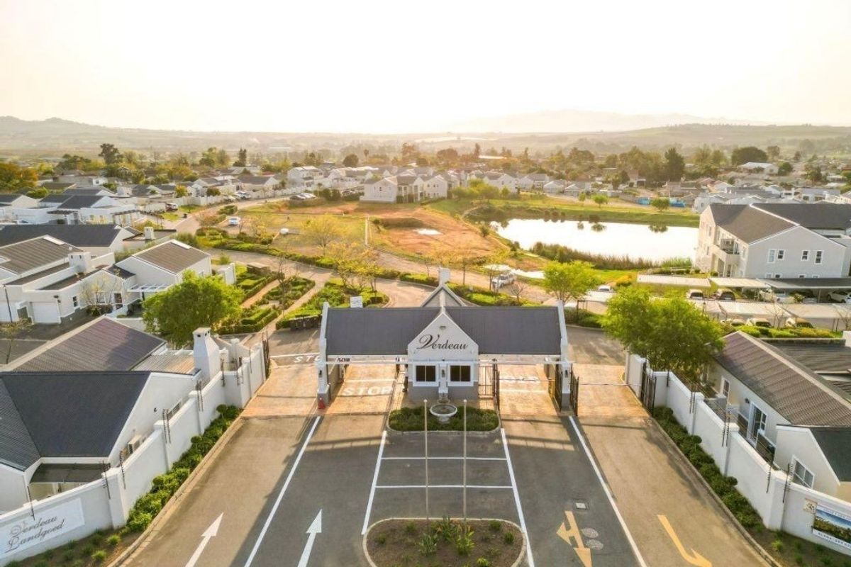 Aerial view of the secure estate entrance featuring a gatehouse, paved access roads, and perimeter security fencing within a landscaped residential development.