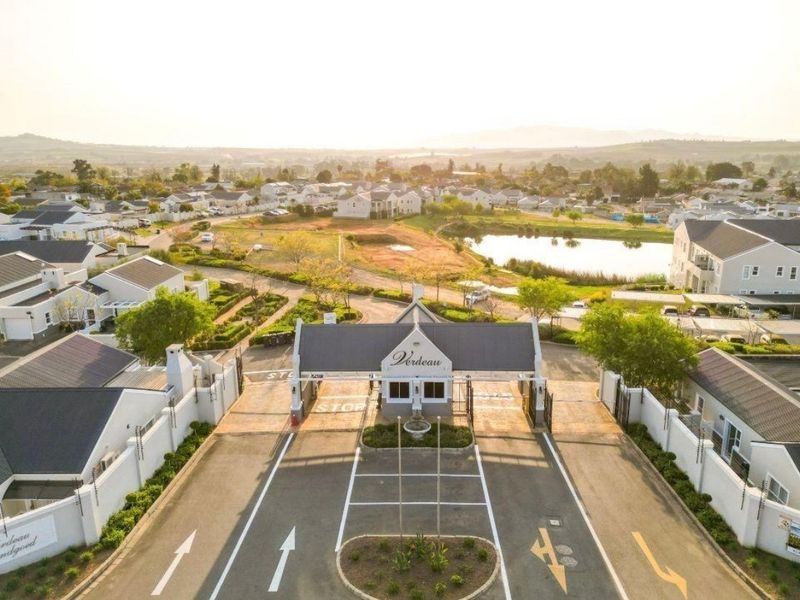 Aerial view of the secure estate entrance featuring a gatehouse, paved access roads, and perimeter security fencing within a landscaped residential development.