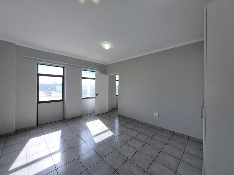 A bright, empty bedroom featuring neutral tiled flooring, built-in cupboards, and large windows allowing for ample natural light.