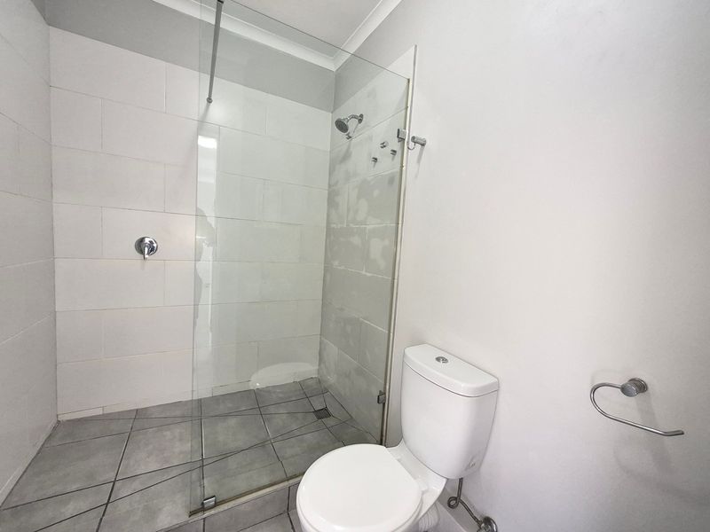 A clean, functional bathroom featuring a glass-enclosed shower, tiled flooring, and a standard toilet, currently awaiting final wall finishing touches.