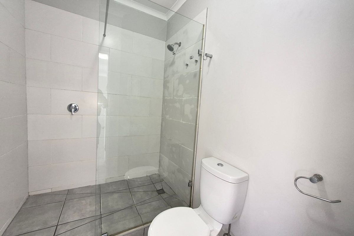A clean, functional bathroom featuring a glass-enclosed shower, tiled flooring, and a standard toilet, currently awaiting final wall finishing touches.