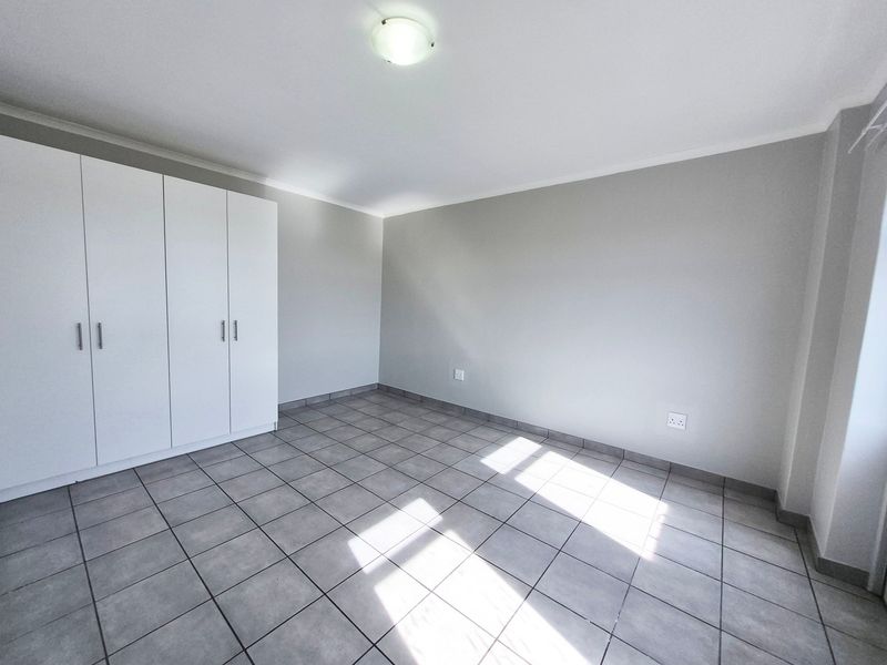 A clean, empty bedroom featuring neutral grey tiled flooring, white built-in cupboards, and a simple ceiling light fixture.