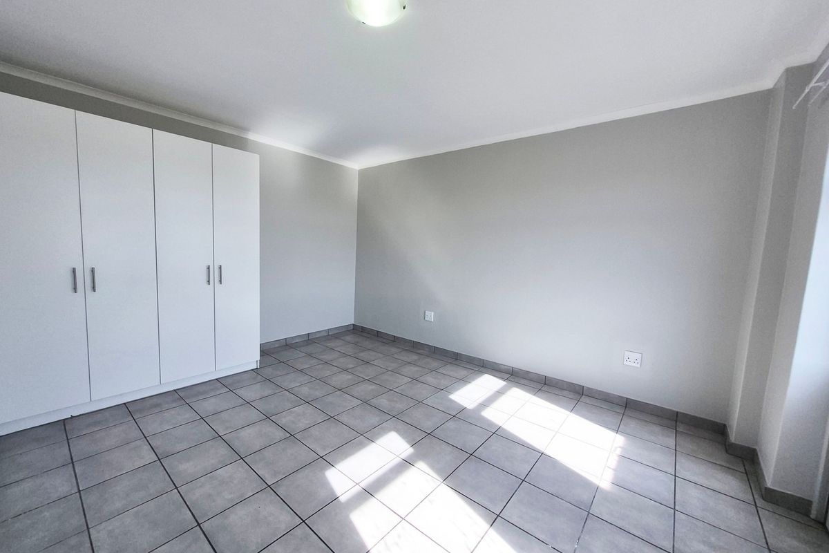A clean, empty bedroom featuring neutral grey tiled flooring, white built-in cupboards, and a simple ceiling light fixture.