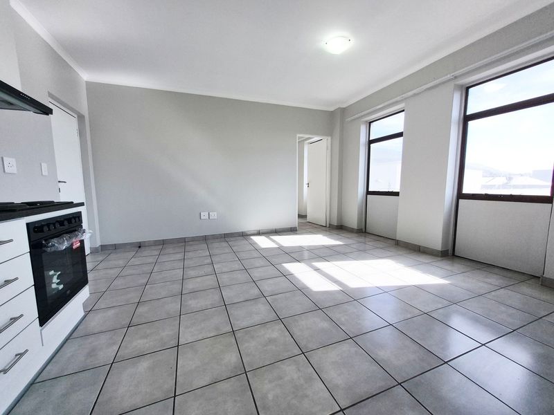 A bright, open-plan living and kitchen area featuring neutral tiled flooring, modern cabinetry, and large windows providing ample natural light.