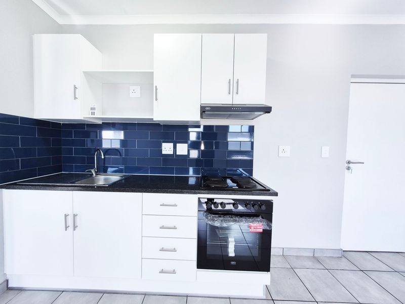 Modern kitchen featuring white cabinetry, dark blue subway tile backsplash, black granite countertops, and integrated stainless steel appliances.