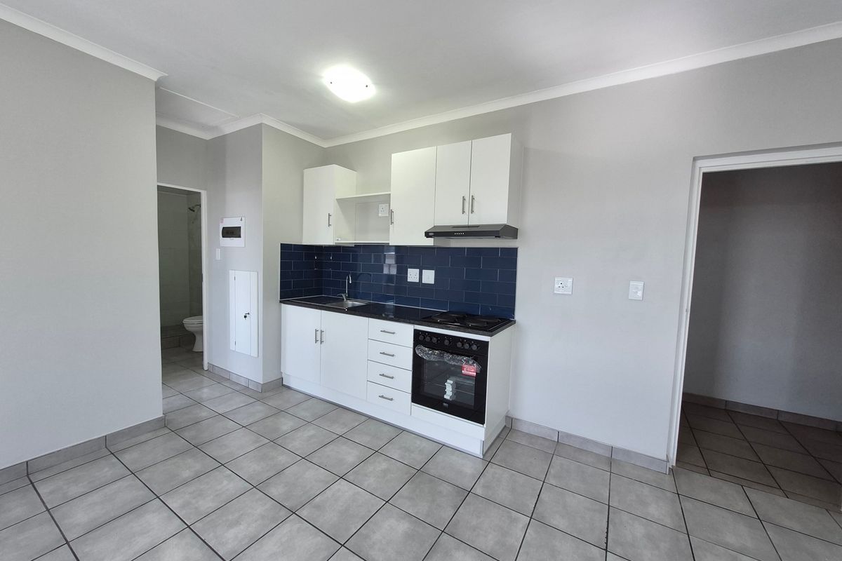 A clean, modern kitchen featuring white cabinetry, dark tiled backsplash, built-in oven and hob, and neutral floor tiles in an open-plan layout.