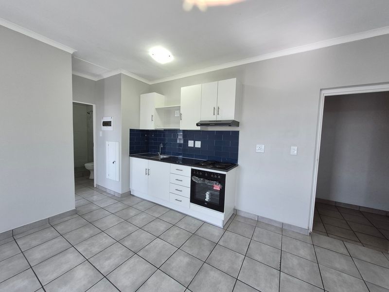 A clean, modern kitchen featuring white cabinetry, dark tiled backsplash, built-in oven and hob, and neutral floor tiles in an open-plan layout.