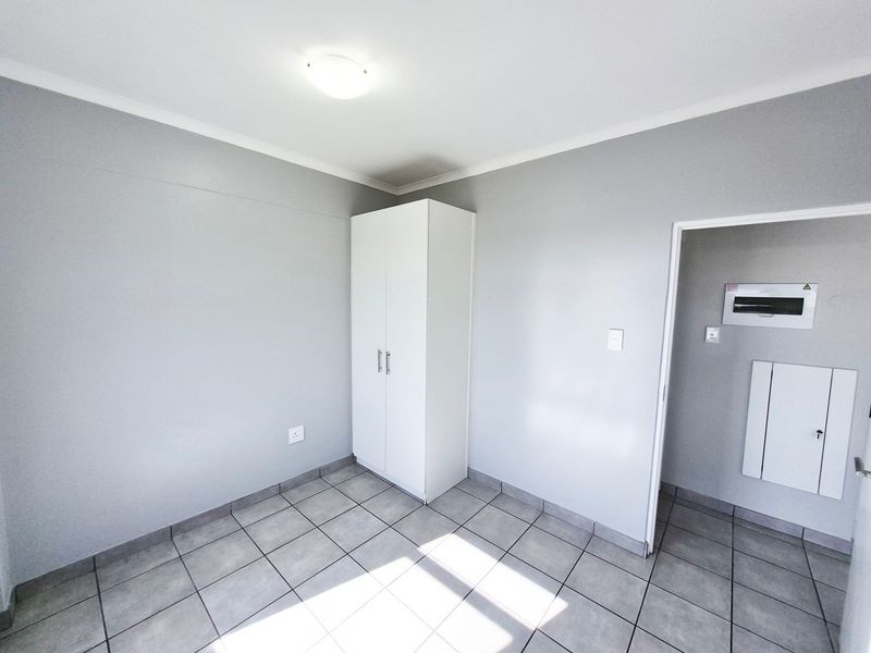 A clean, neutral bedroom featuring tiled flooring, a built-in wardrobe, and a functional layout with an adjacent utility area.