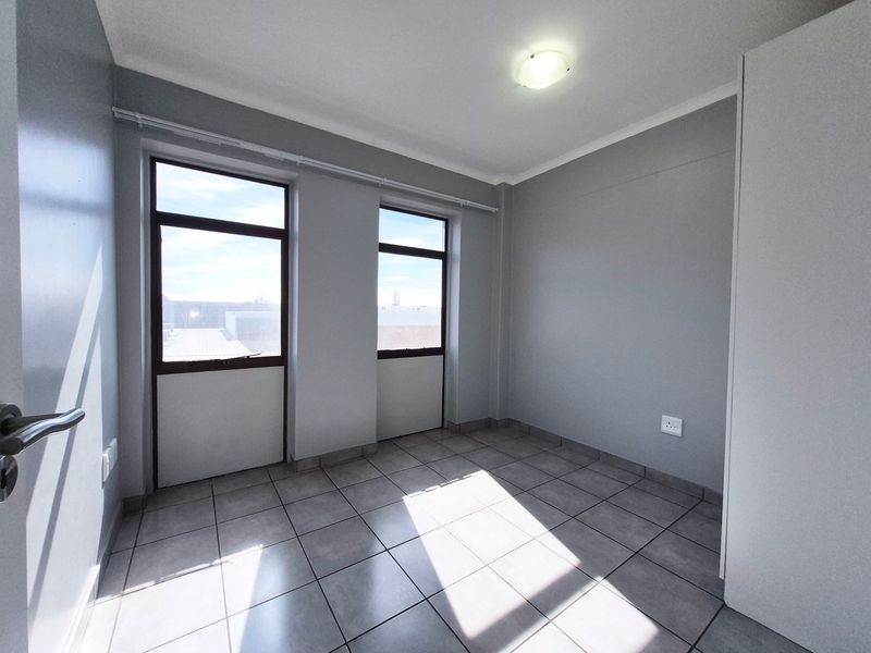 A bright, empty bedroom featuring neutral grey walls, tiled flooring, and a built-in cupboard, offering a clean and versatile space.