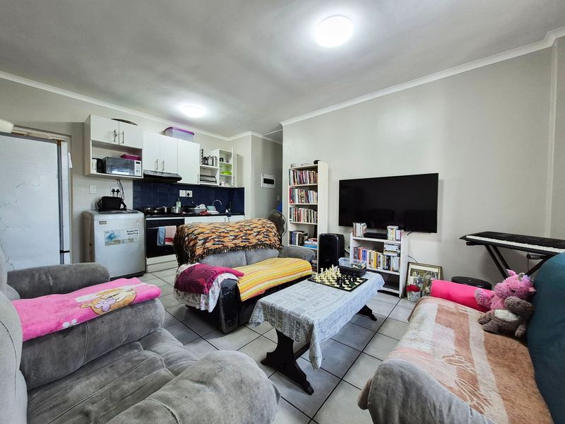 Open-plan living area featuring a functional kitchen with built-in cabinetry, oven, and hob, seamlessly connected to the main living space with tiled flooring throughout.