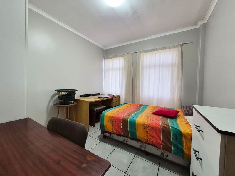 A functional bedroom featuring tiled flooring and neutral wall finishes, providing a practical space with natural light from the window.