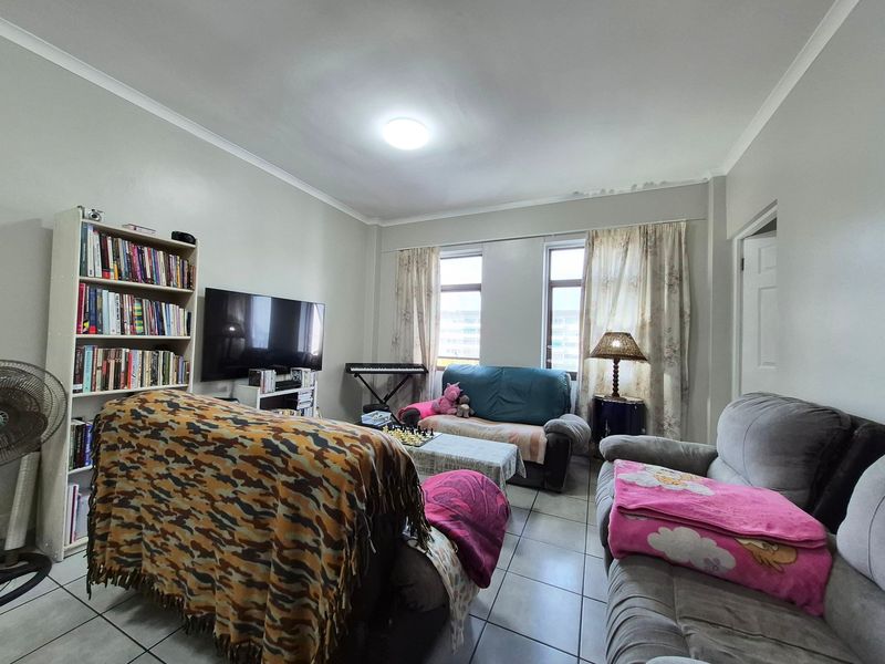 A functional living room featuring tiled flooring, dual windows for natural light, and coved ceiling detailing.