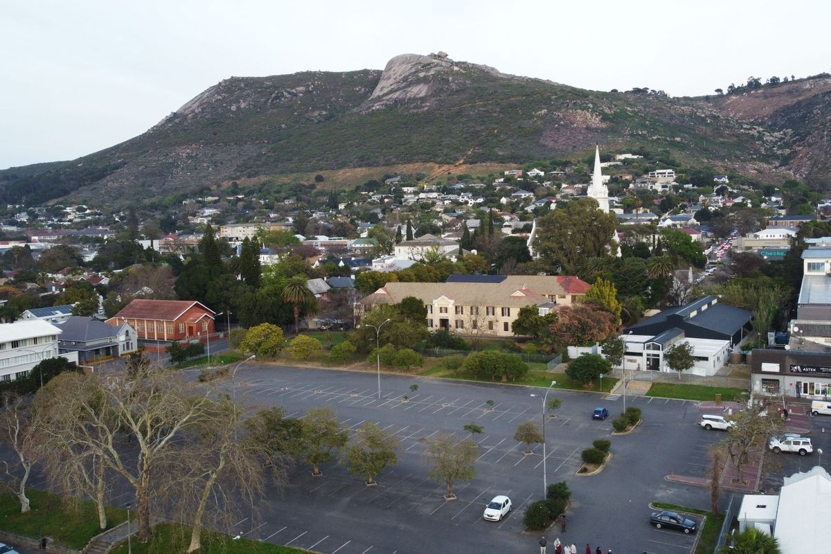 An aerial view of the surrounding neighbourhood, featuring a large parking area, local buildings, and a prominent mountain backdrop.