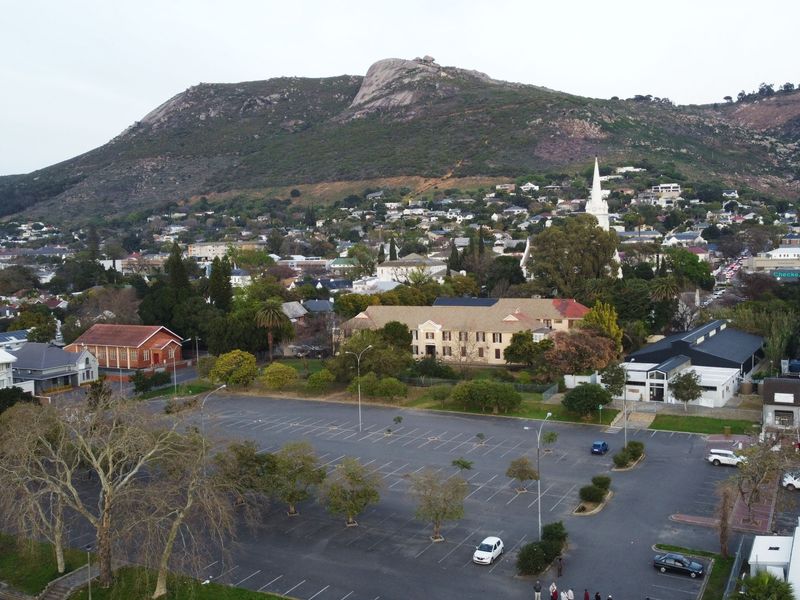 An aerial view of the surrounding neighbourhood, featuring a large parking area, local buildings, and a prominent mountain backdrop.