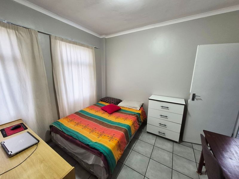 A functional bedroom featuring tiled flooring, neutral wall paint, and large windows with curtain rails, providing a simple and practical living space.