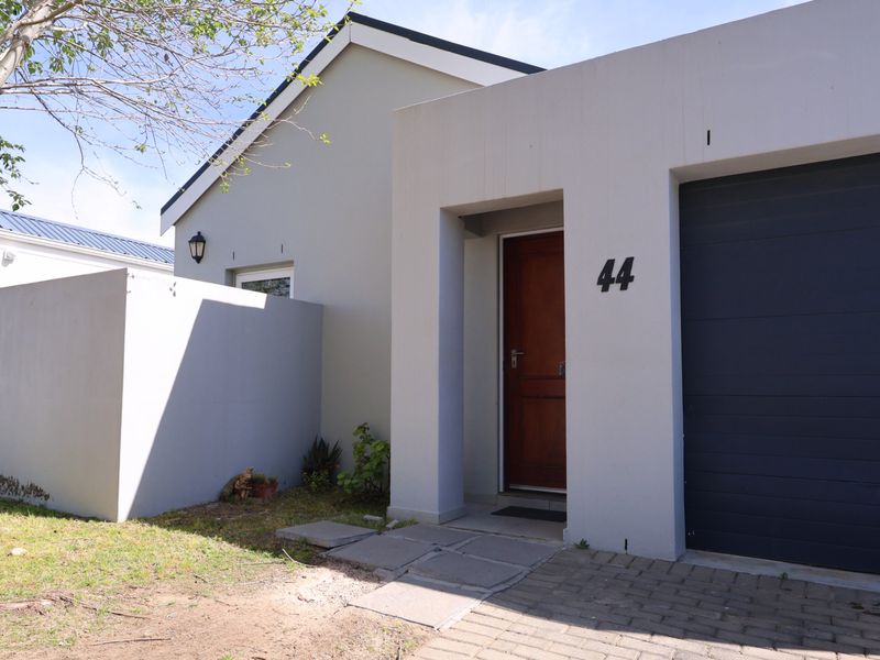 Front elevation of the property featuring a paved driveway, a single garage, and a private entrance with a wooden door.