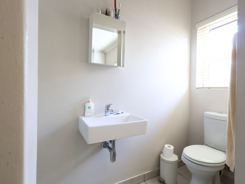 A functional guest bathroom featuring a wall-mounted basin, chrome fixtures, a mirrored medicine cabinet, and a standard toilet.