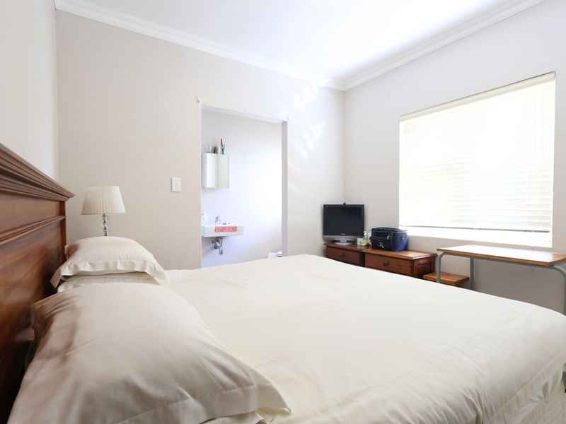 A bedroom featuring neutral walls, crown molding, and a window with venetian blinds, with an adjoining small en-suite area containing a wall-mounted basin.
