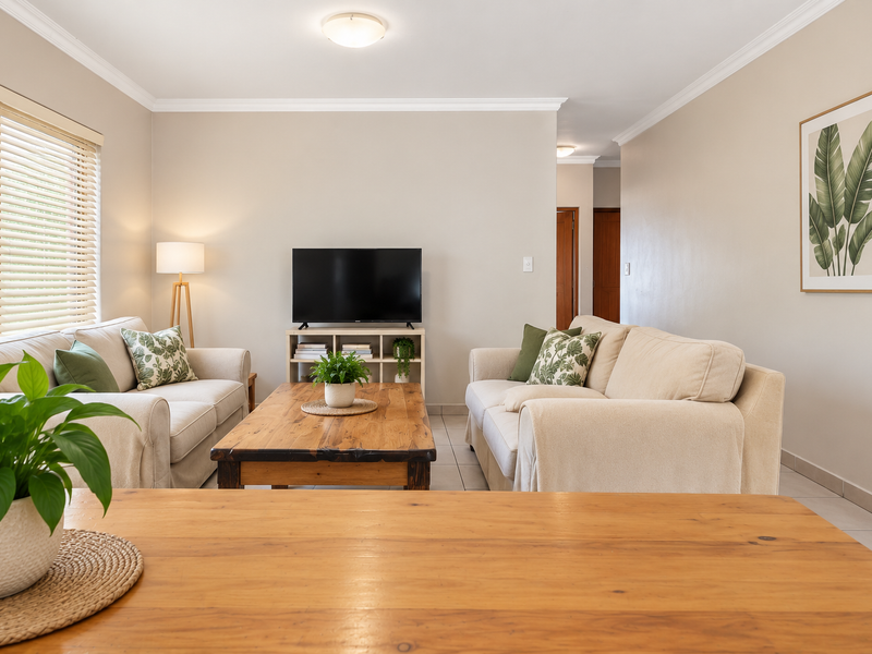 A well-maintained living room featuring neutral wall tones, tiled flooring, and venetian blinds, providing a bright and comfortable space.