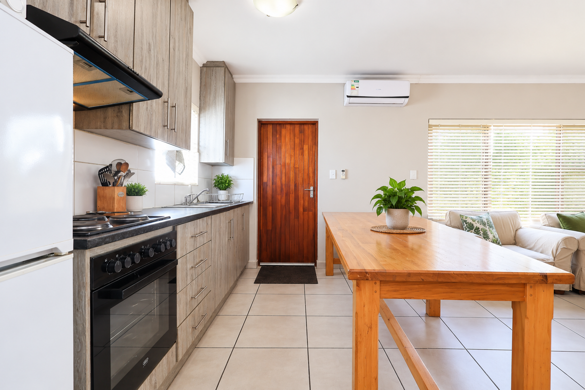Open-plan kitchen and living area featuring modern wood-look cabinetry, built-in appliances, tiled flooring, and a split-system air conditioner.