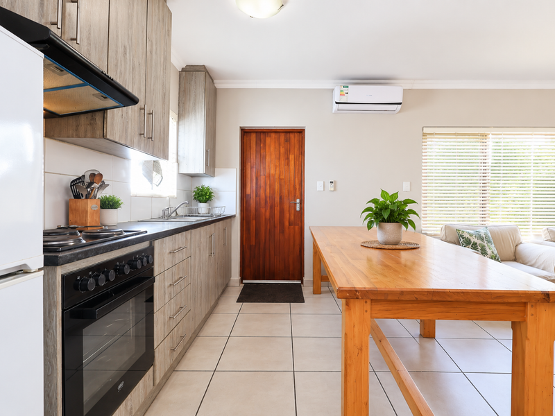Open-plan kitchen and living area featuring modern wood-look cabinetry, built-in appliances, tiled flooring, and a split-system air conditioner.