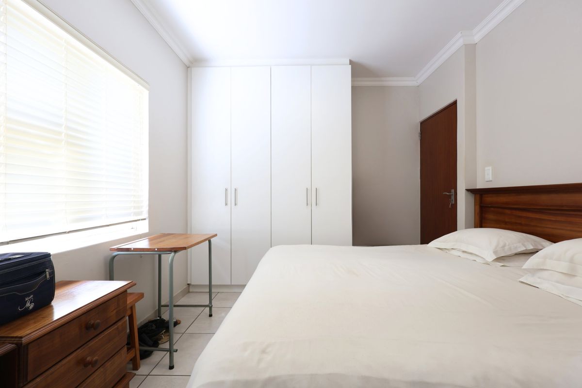 A well-maintained bedroom featuring neutral tiled flooring, built-in white cupboards, and venetian blinds, offering a clean and functional living space.
