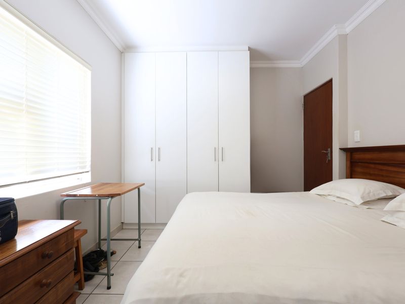 A well-maintained bedroom featuring neutral tiled flooring, built-in white cupboards, and venetian blinds, offering a clean and functional living space.